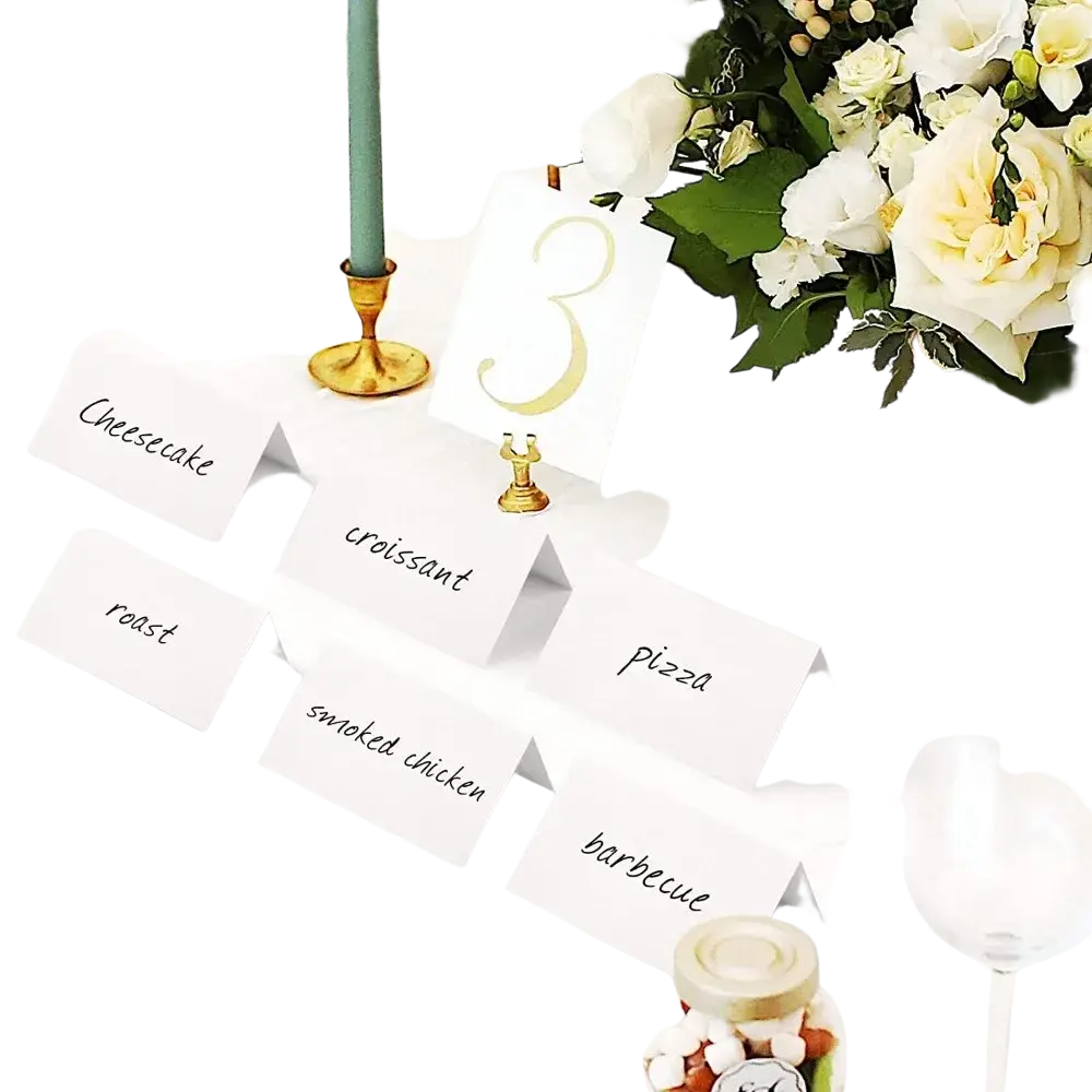 White paper eucalyptus leaf place cards with black cursive text arranged on a wedding table setting