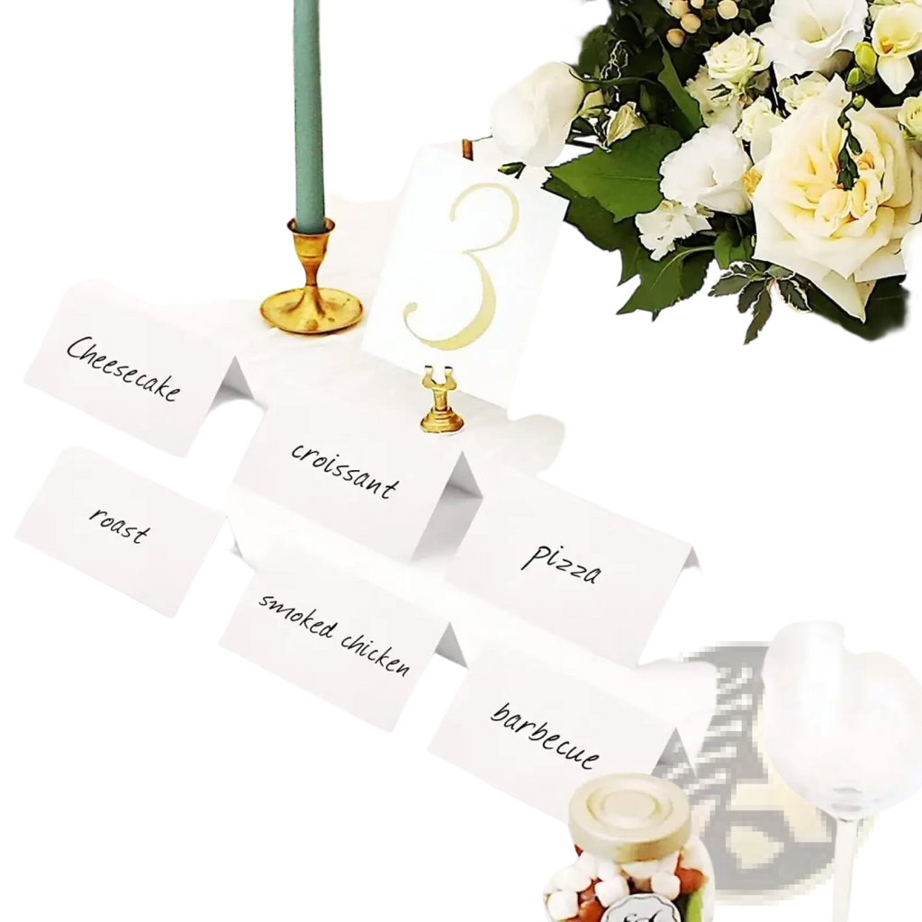 White paper eucalyptus leaf place cards with black cursive text arranged on a wedding table setting