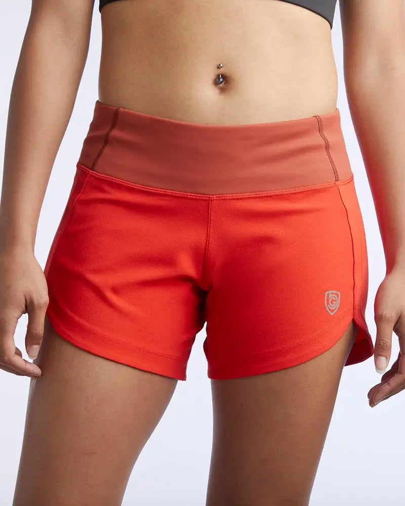 Bright orange women’s athletic shorts with rust high-waisted waistband and shield logo for workout use