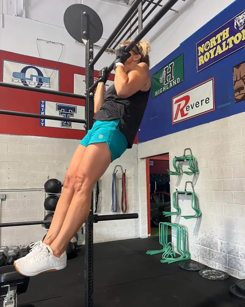 A woman performs pull-ups wearing Excel women’s black camouflage athletic workout shorts and white athletic shoes