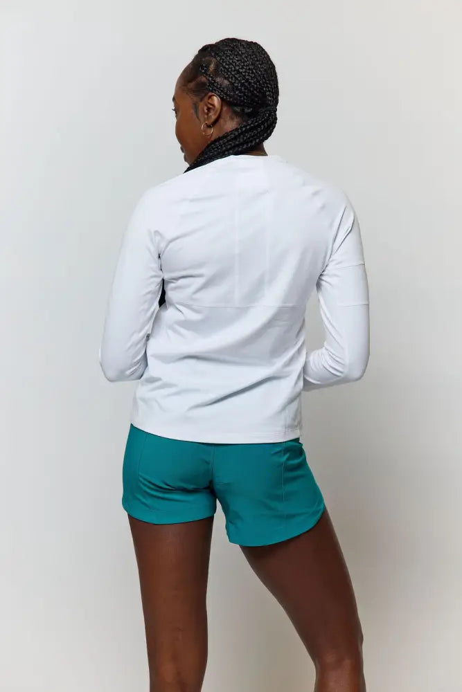 Woman wearing white long-sleeved athletic top with teal shorts paired with excel women’s black camouflage workout shorts