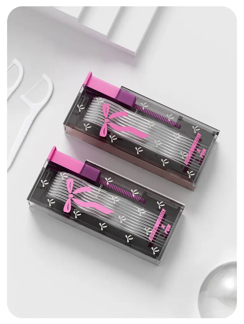 Porta-picks para hilo dental tipo palillo con dispensador automático de apertura emergente en cajas portátiles para hilo dental, en rosa y negro, con lazos decorativos para un uso conveniente en la higiene bucal.