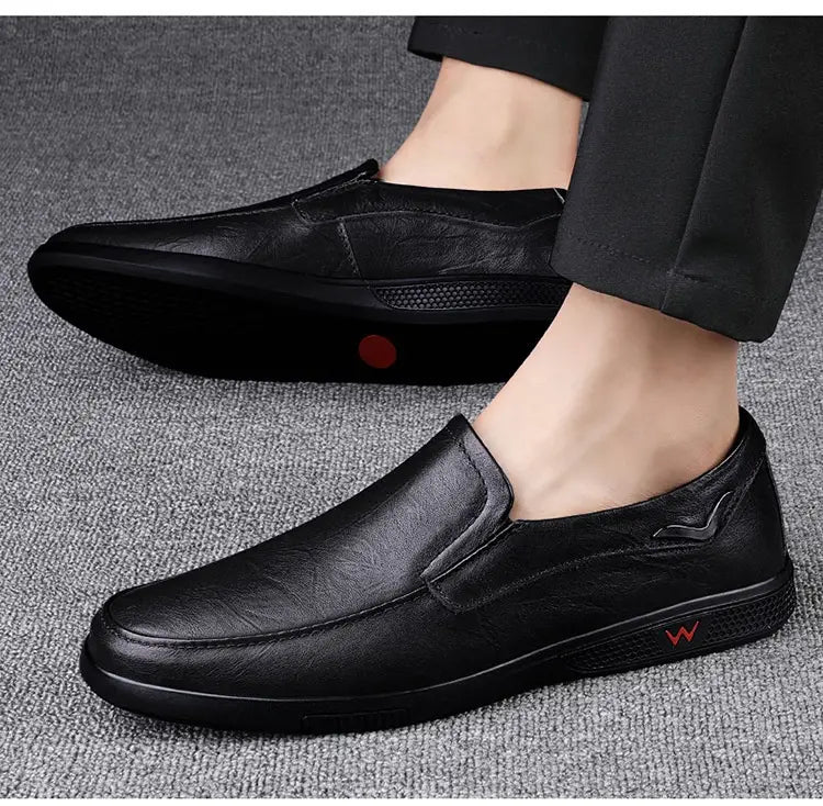 Mocassins noirs à enfiler pour homme en cuir avec un discret logo rouge sur le côté et des semelles en caoutchouc texturées, style britannique.