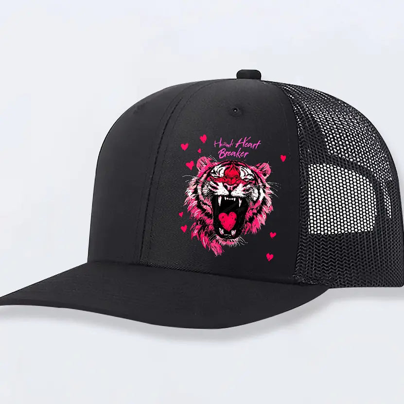 Black trucker hat featuring a vibrant pink tiger graphic with an open mouth and heart-shaped tongue surrounded by small hearts and the text heart breaker in matching pink, designed for men in tan material.