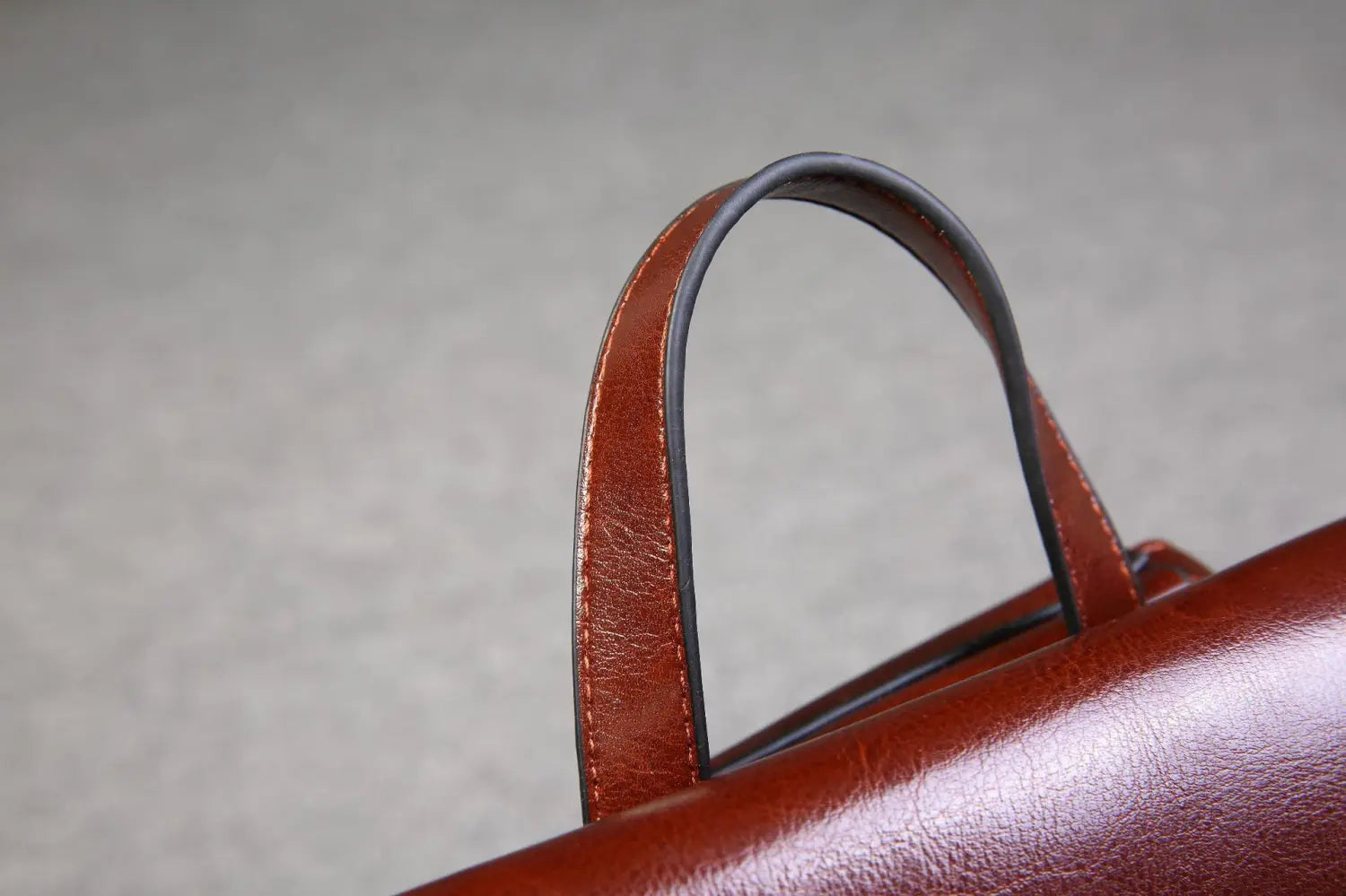 Asa de cuero marrón con acabado liso ligeramente brillante y costuras visibles a lo largo de los bordes en un bolso bandolera de cuero estilo moda retro.