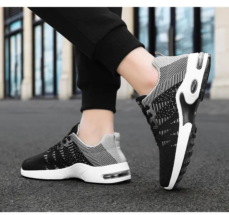 Baskets décontractées pour hommes en mesh flyknit à coussin d’air, en noir et gris, en tricot mesh, avec semelle intermédiaire blanche et unités d’amorti par coussin d’air visibles.