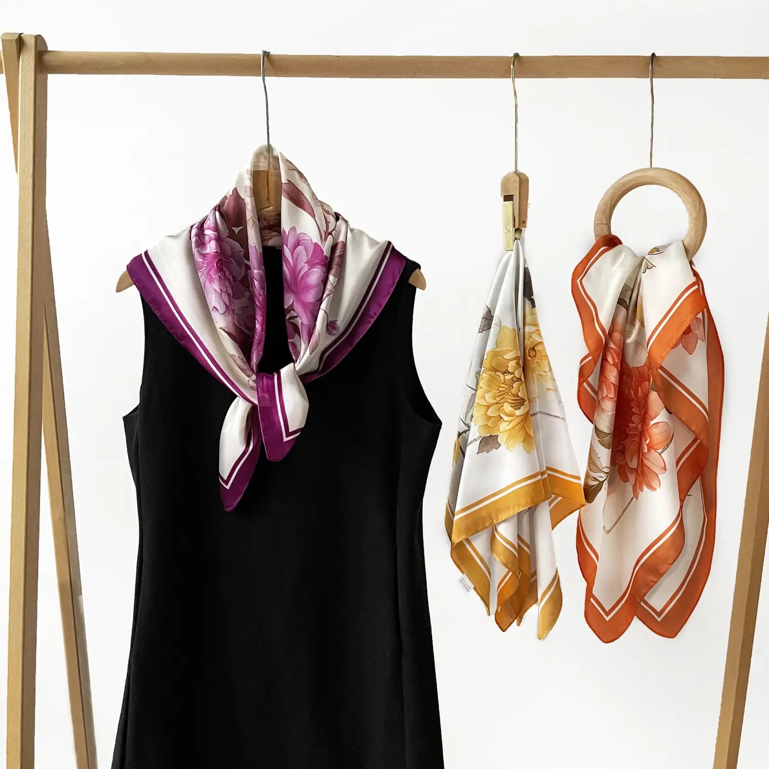 A delicate pink and white floral silk square scarf with a purple border elegantly draped over a black dress.