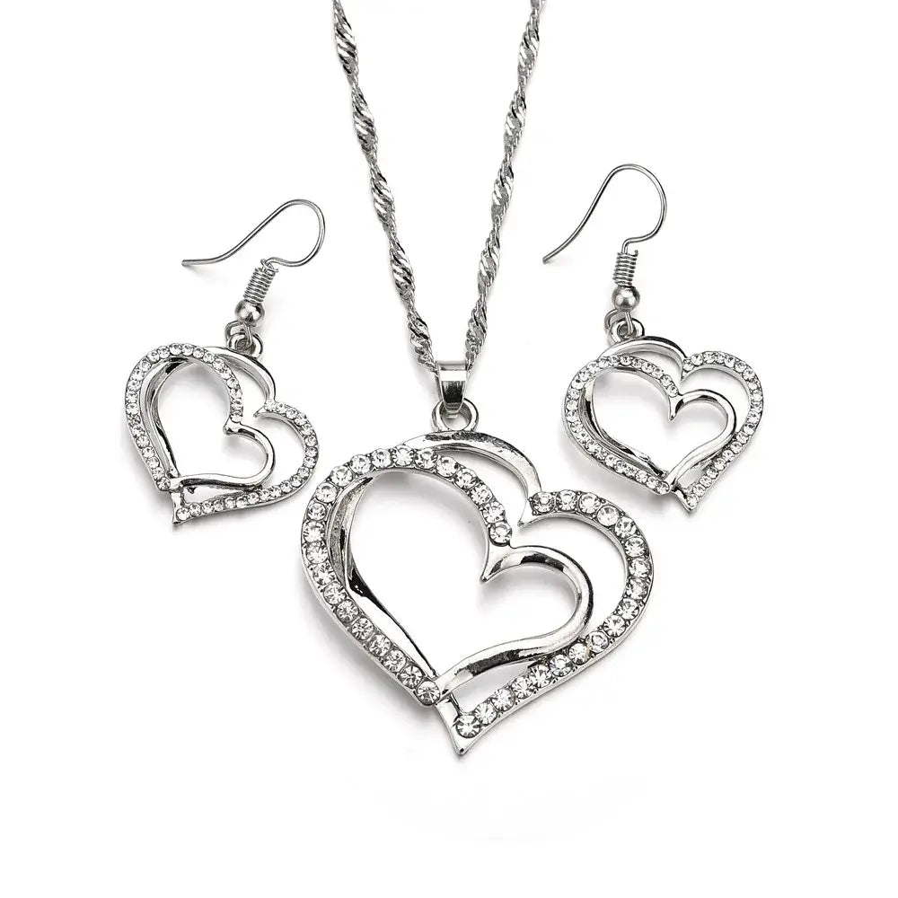Elegant rhinestone heart jewelry set featuring a silver heart-shaped pendant necklace with a twisted chain and matching rhinestone-detailed earrings.