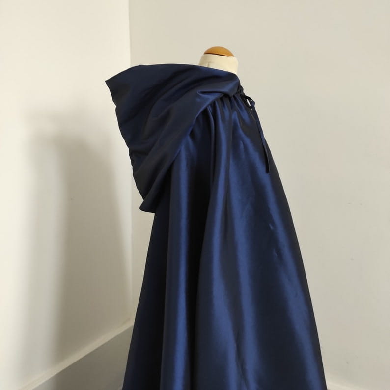 a deep navy satin cape with a hood and drawstring closure displayed alongside a wooden cat tree scratching post and condo