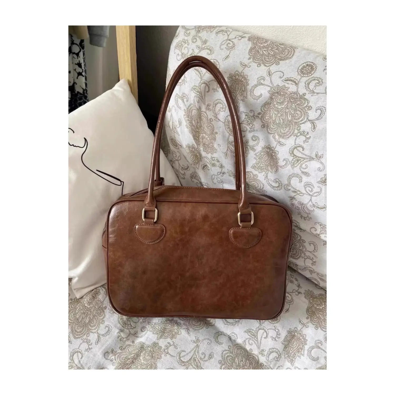 Brown leather handbag with rounded top handles and metallic hardware featuring a large capacity design and a bear charm.