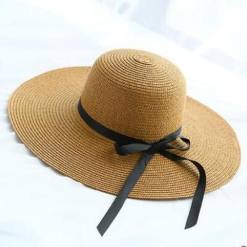 Beige wide brim straw sun hat featuring a black ribbon tied in a bow around the crown.