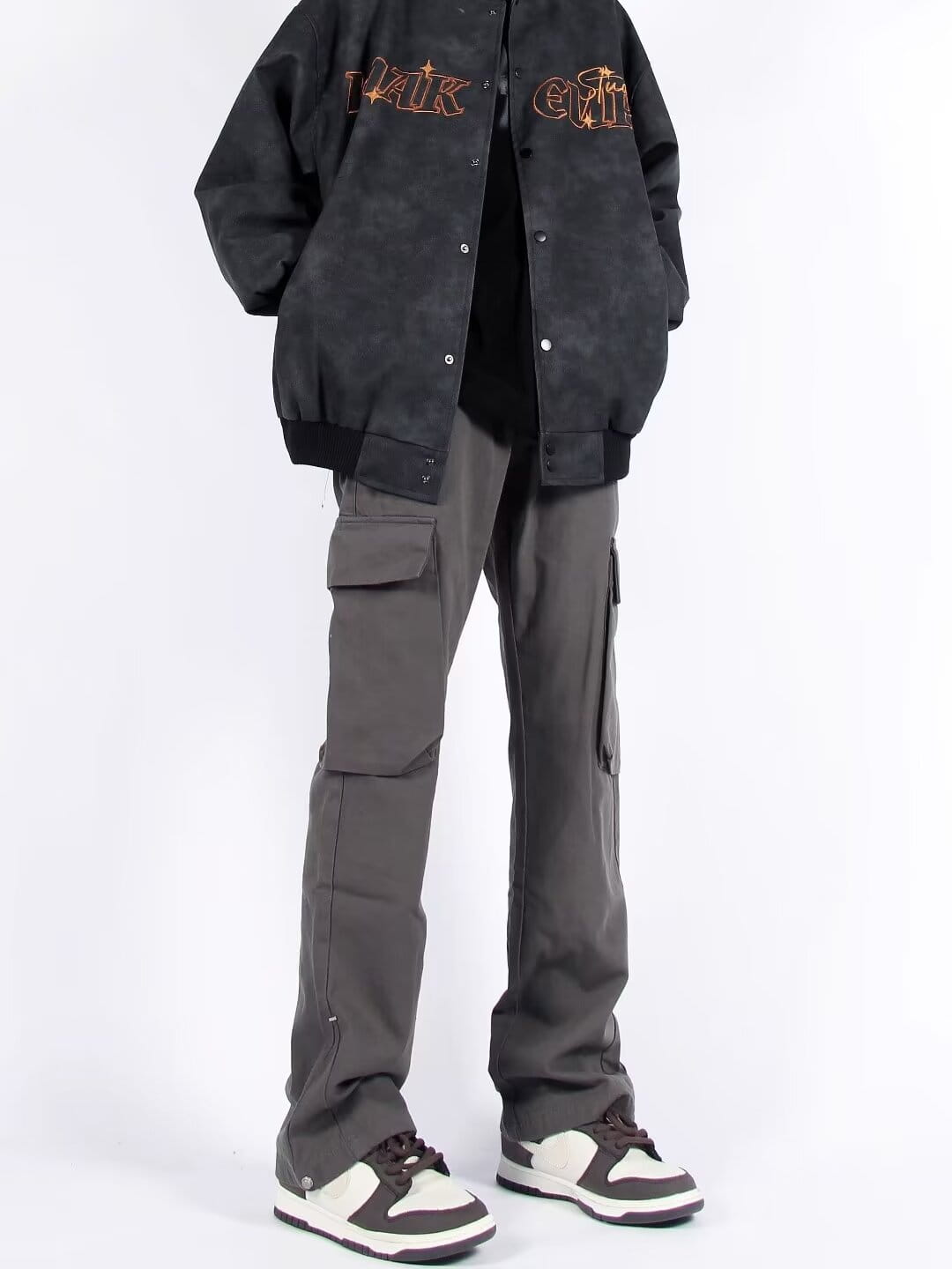 Chaqueta bomber negra con letras bordadas naranjas en el pecho y las mangas, combinada con pantalones cargo rectos de pierna recta con múltiples bolsillos.