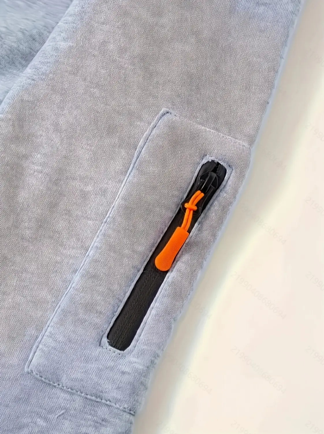 Gray heathered fabric pants feature a side pocket with an orange zipper pull paired with a men’s sport casual fleece lined zipper hoodie jacket.