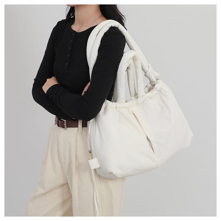 White quilted puffer tote bag made of lightweight nylon with thick padded shoulder handles and a drawstring closure.