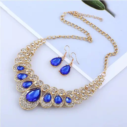 Vintage gold teardrop crystal bridal jewelry set featuring a gold-toned necklace with cascading royal blue teardrop stones and clear crystals paired with matching earrings.
