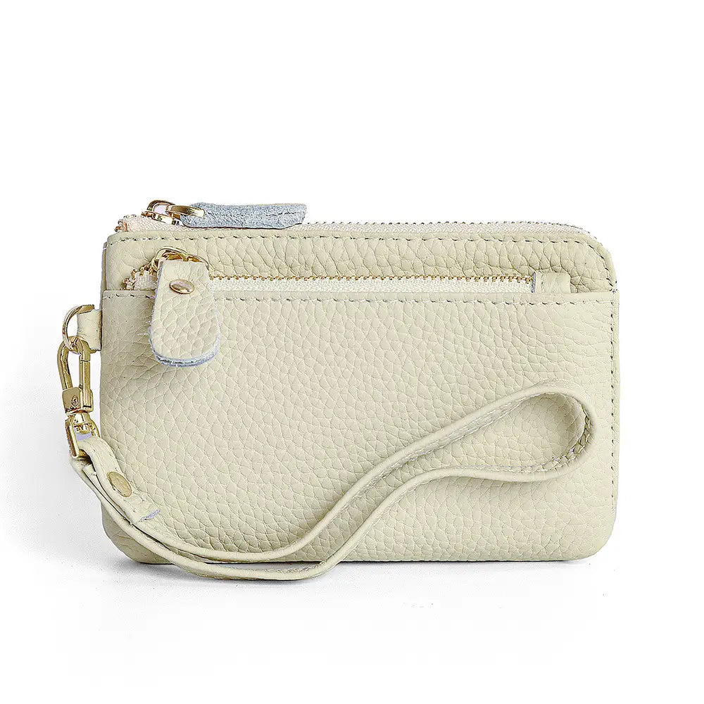 Cream-colored textured leather wristlet wallet with gold hardware and a matching adjustable strap.