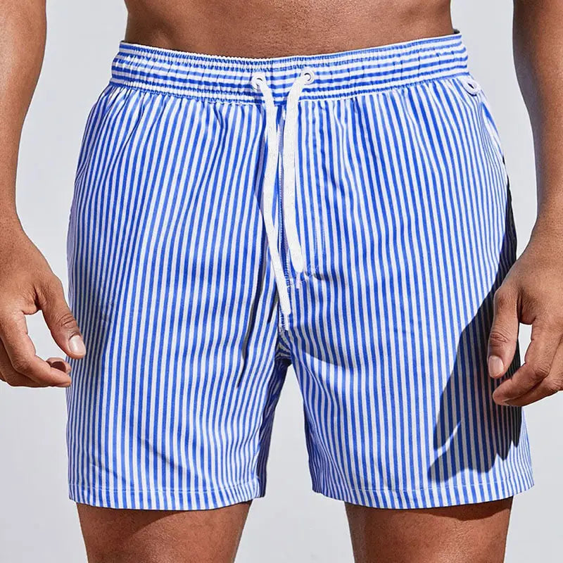 Men’s striped tropical print swim trunks featuring blue and white vertical stripes with an elastic waistband and white drawstring.