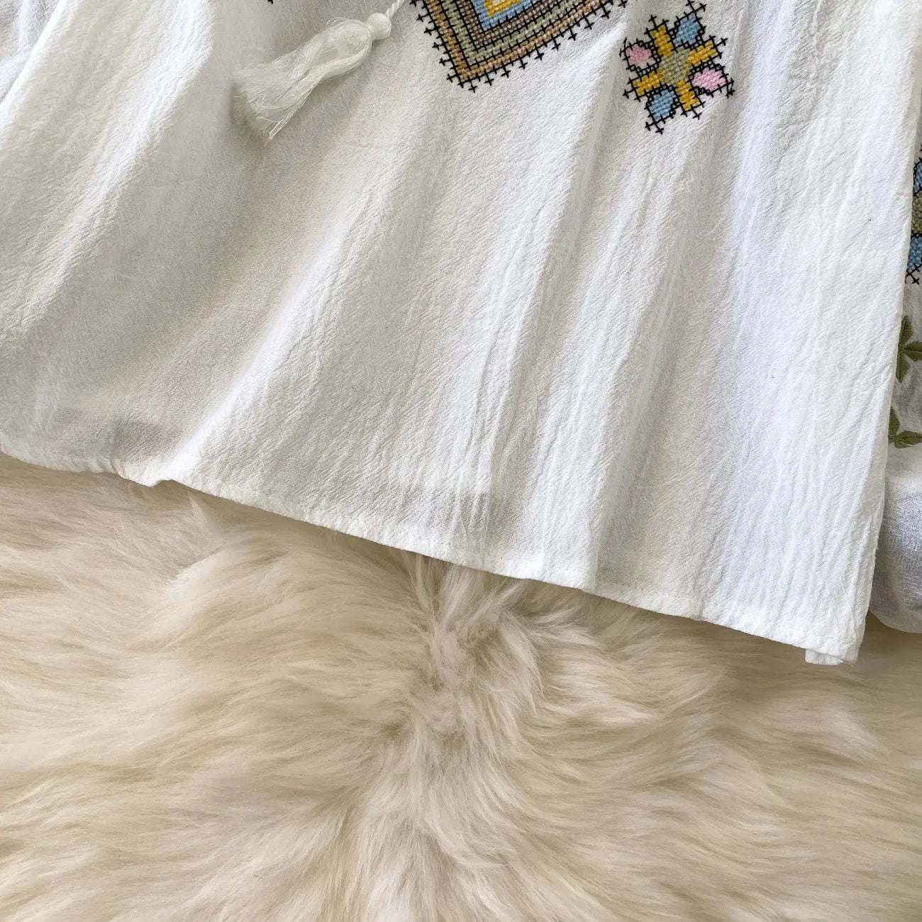 White linen embroidered lantern sleeve tie neck blouse with intricate pastel cross-stitch embroidery and decorative tassel