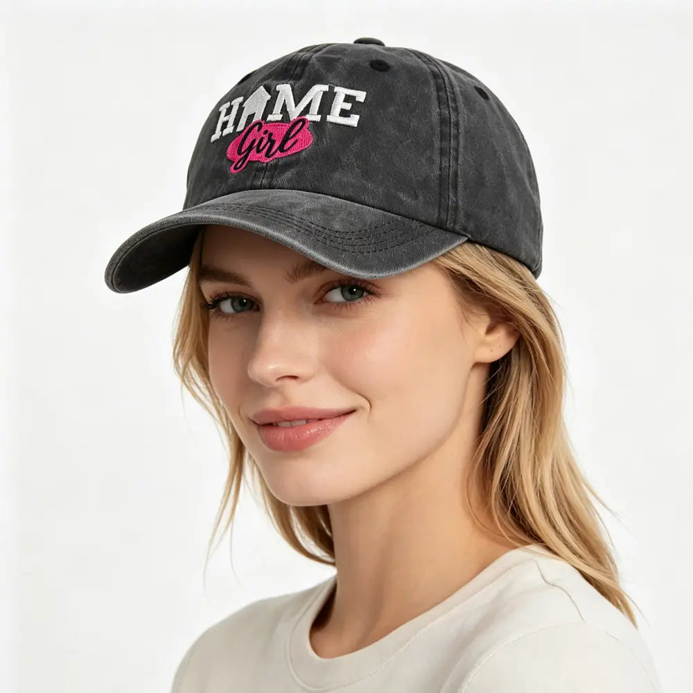 Casquette de baseball délavée et usée en gris foncé, brodée avec « home girl » en blanc et en lettres roses.