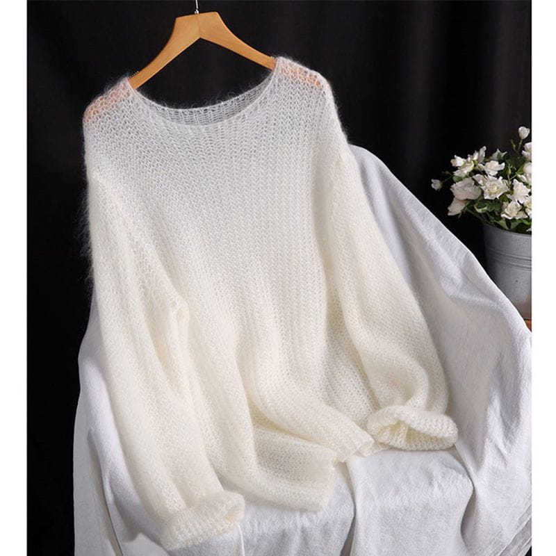 Ein weiches off-weißes Pulloveroberteil in offener Strickoptik, als Blusenstil gestricktes Oberteil, mit lockerer Passform und weiten Ärmeln aus flauschigem Strickmaterial, hängt auf einem Holzkleiderbügel.
