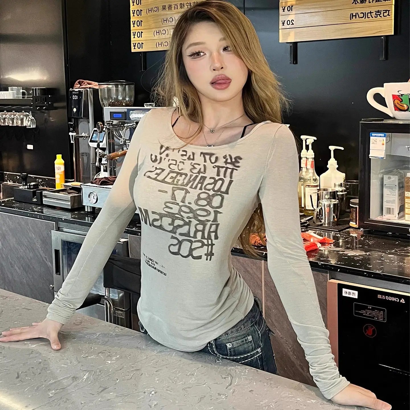 A light gray long-sleeved sheer crop top featuring bold black graphic letter print across the chest.