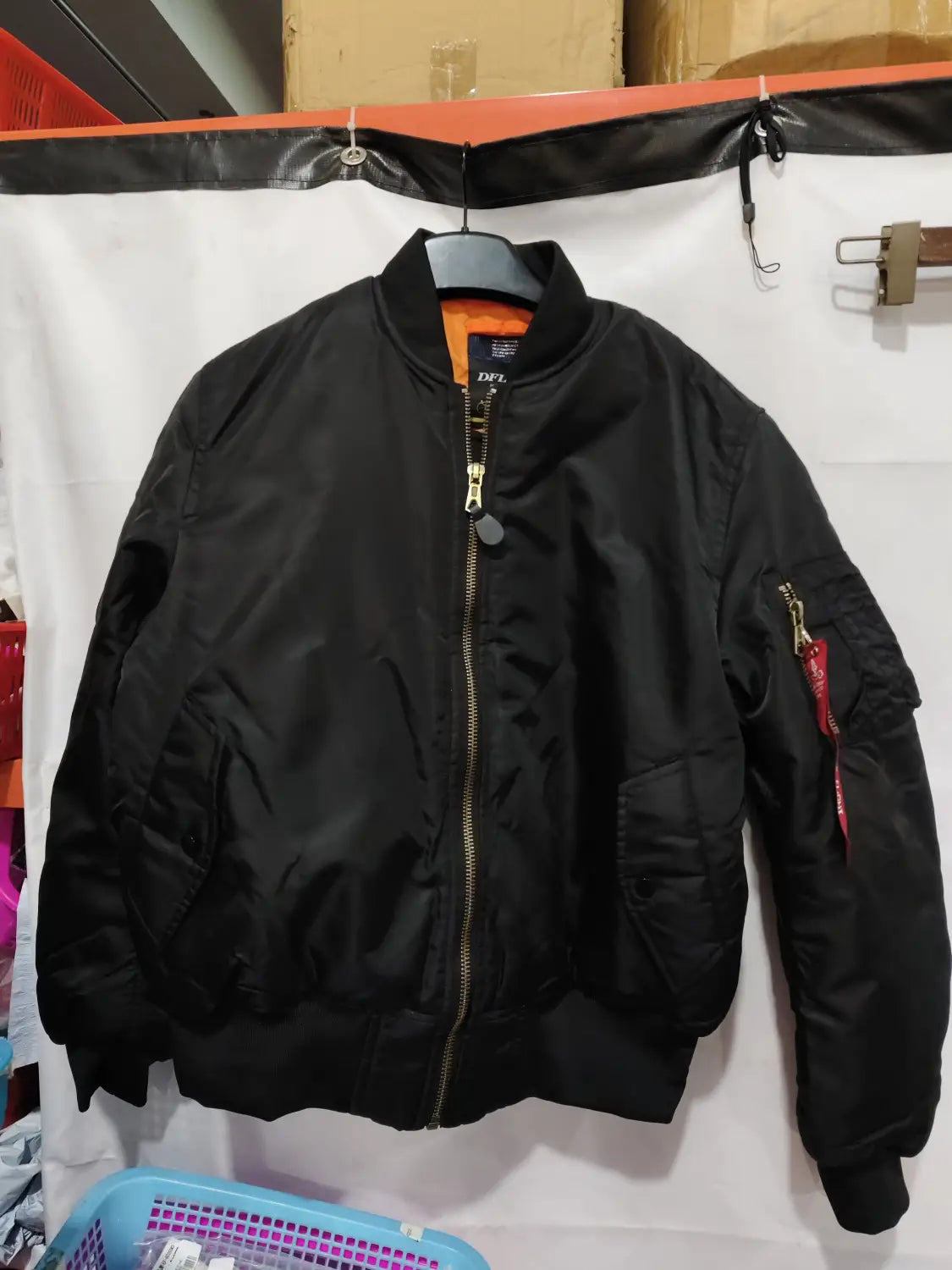 Men’s pilot cotton bomber jacket in black featuring a gold zipper and a red tag on the sleeve hanging on a hanger.
