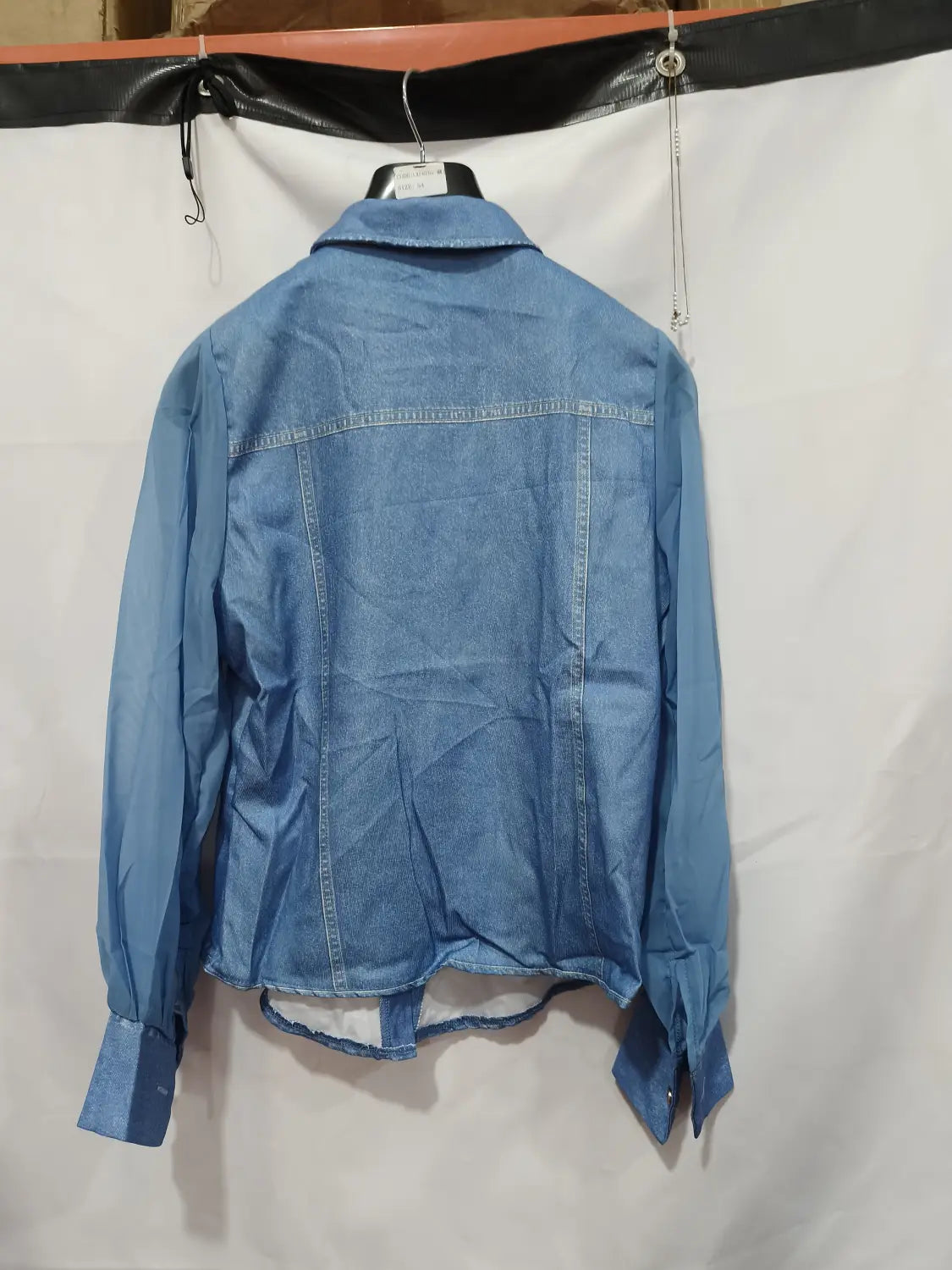 Une veste en denim bleu à lavage moyen, avec col classique et poignets boutonnés, complétant un haut à encolure en V à manches transparentes en denim.