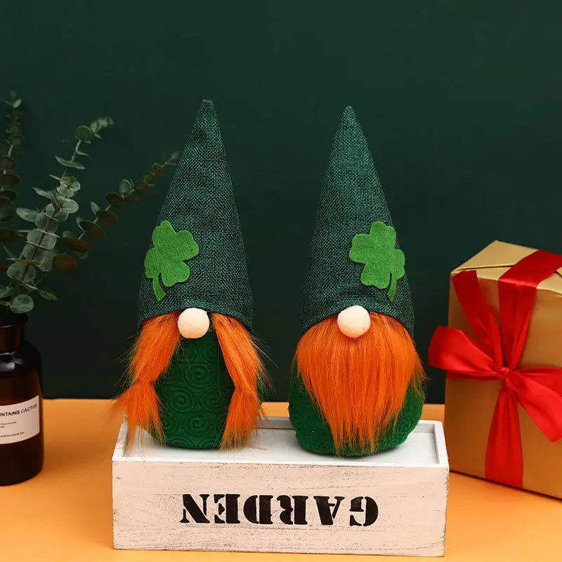 Zwei identische St.-Patrick’s-Day-Leprechaun-Gnome-Plüschpuppen aus grünem Stoff mit orangefarbenen flauschigen Bärten und Kleeblatt-Applikationen auf spitzen Hüten sitzen nebeneinander.