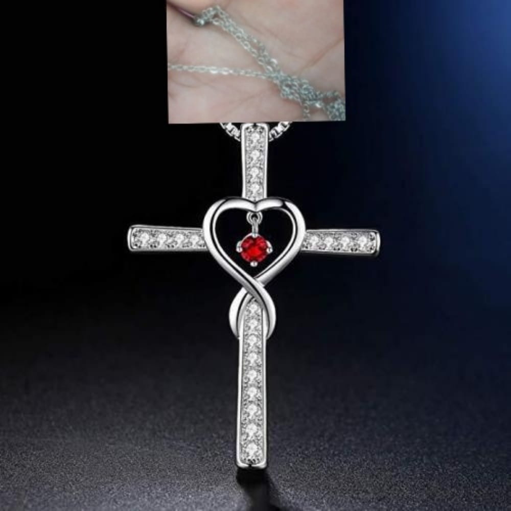 Silver cross pendant necklace featuring a heart-shaped center with a red birthstone gemstone and clear crystals along the arms, named infinity love heart cross birthstone crystal necklace.