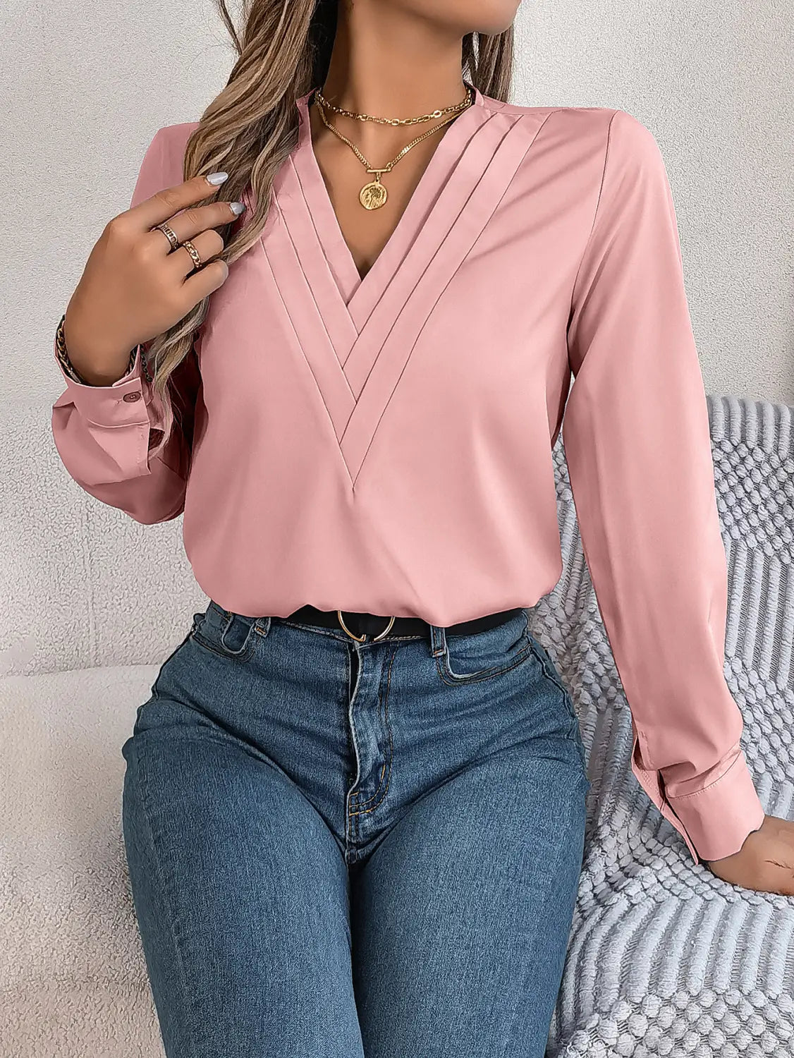 A soft pink long-sleeved blouse with v-neck and pleated front detail similar to the white satin v neck wrap blouse with black trim.