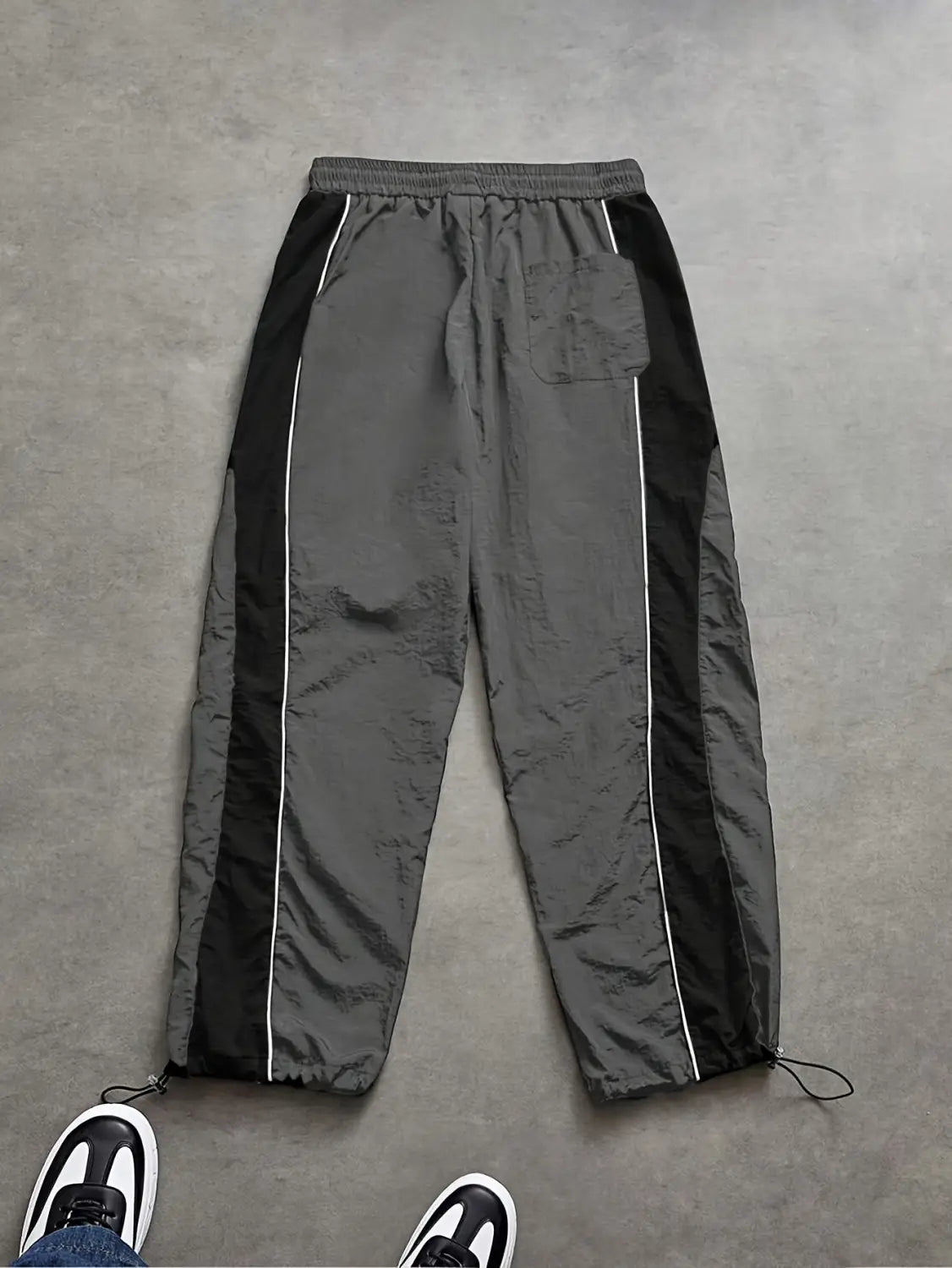 Men quick dry athletic track pants in gray and black with white piping along side panels, featuring a drawstring waistband and adjustable ankle cords.