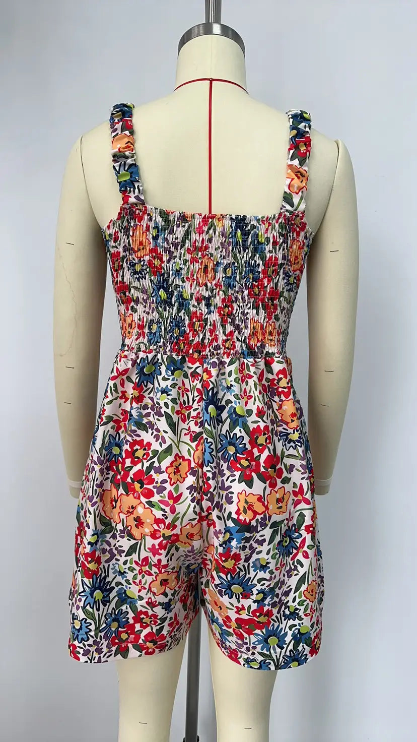 Mono tipo peto de estampado floral sin mangas para playa de verano, con espalda fruncida y tirantes de hombro ajustables; presenta flores rojo, naranja, azul y verde sobre un fondo blanco.