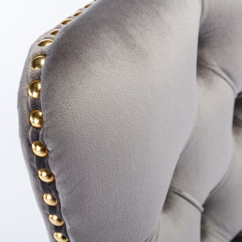 Accoudoir en velours gris avec garniture à clous décoratifs ton sur ton or sur une chaise de bureau en velours gris capitonné avec piètement pivotant à base ton sur ton or.