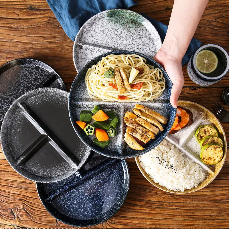 Service d’assiettes de dîner divisées en céramique avec glaçure à mouchetures, comprenant une assiette en céramique noire à mouchetures avec quatre compartiments, chacun recevant différents aliments.
