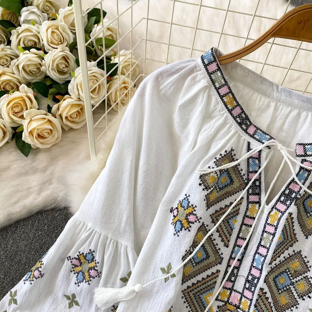 White embroidered lantern sleeve tie neck blouse with intricate geometric embroidery in pastel pink blue yellow and brown threads.
