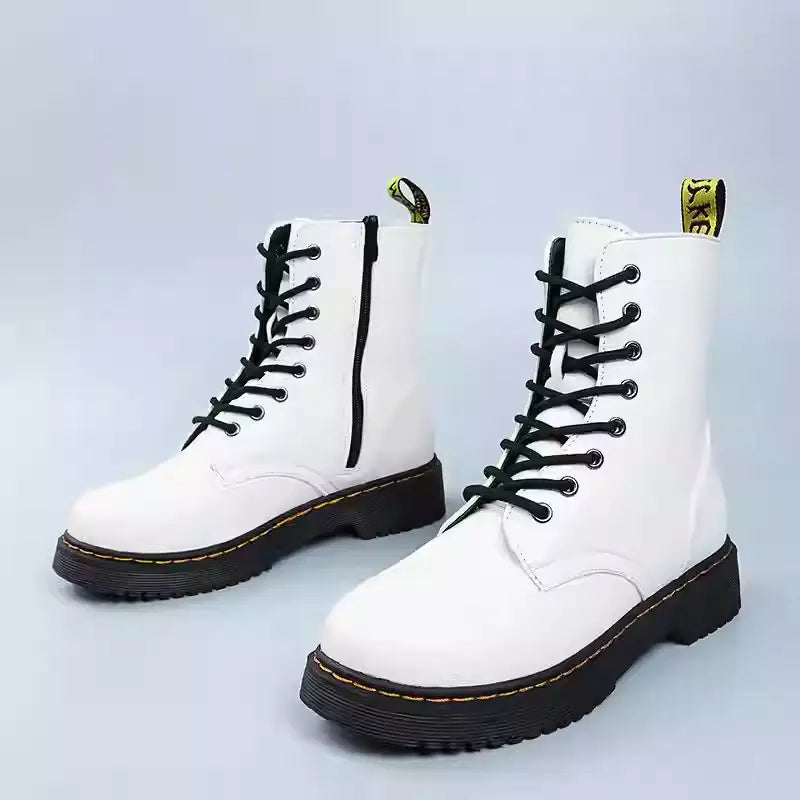 Botines estilo Martin de cuero blanco con punta redonda, calzado plano a la altura del tobillo, con cordones negros y una lengüeta de extracción amarilla, mostrados desde el lado trasero
