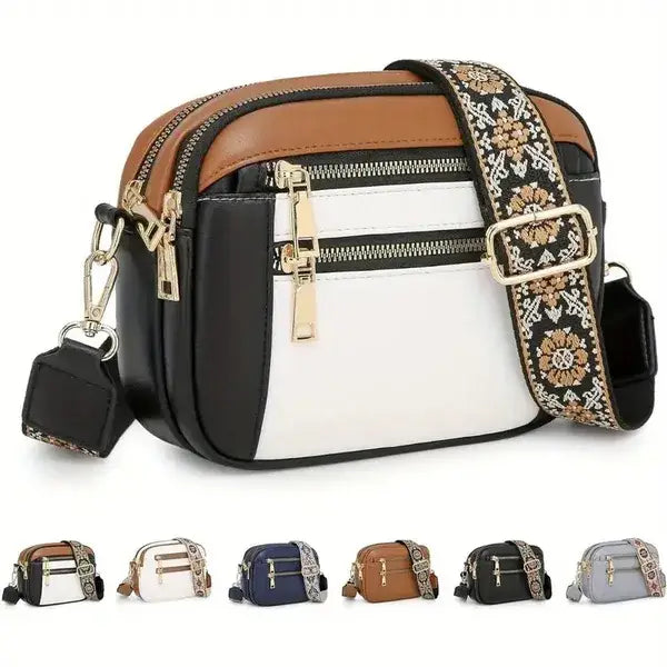 A stylish colorblock leather crossbody bag featuring a black white and tan design with gold-tone zippers and an ornate floral-patterned strap.