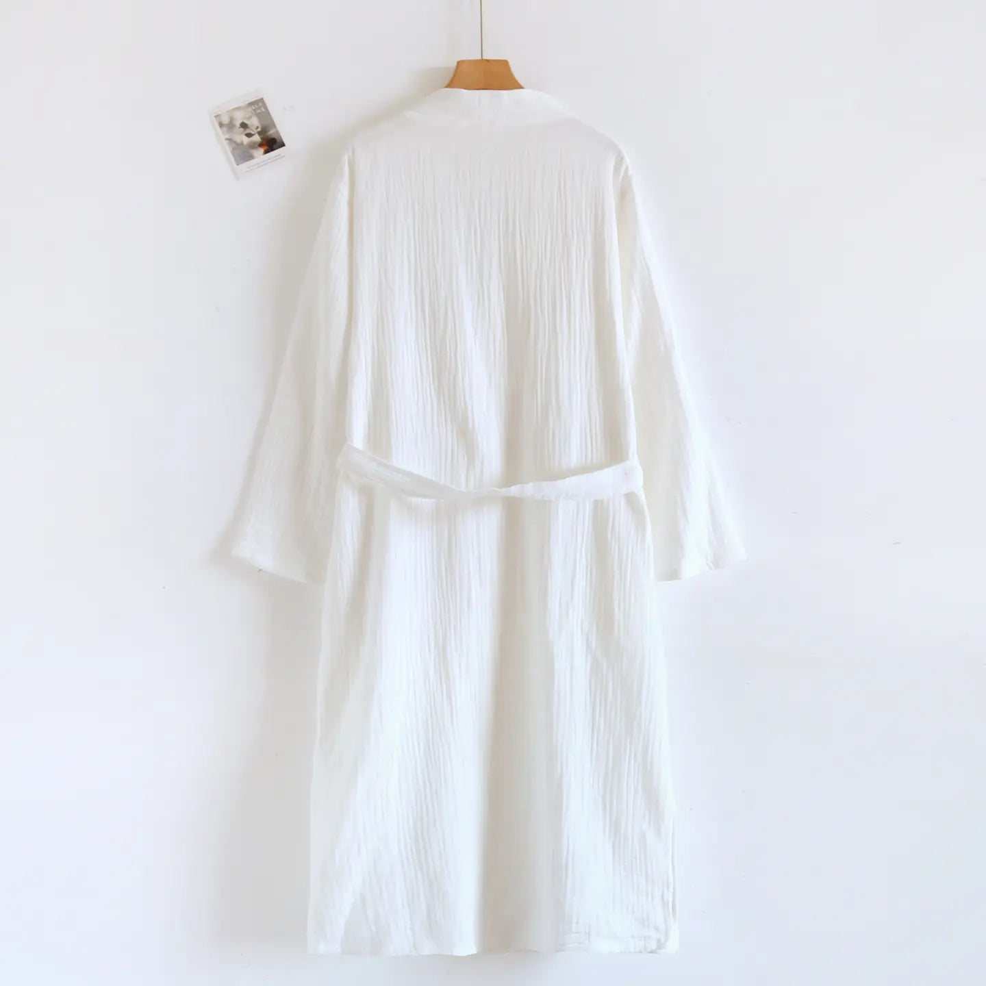Peignoir en gaze de coton texturée blanc pour homme, avec une ceinture assortie suspendue sur un cintre en bois.