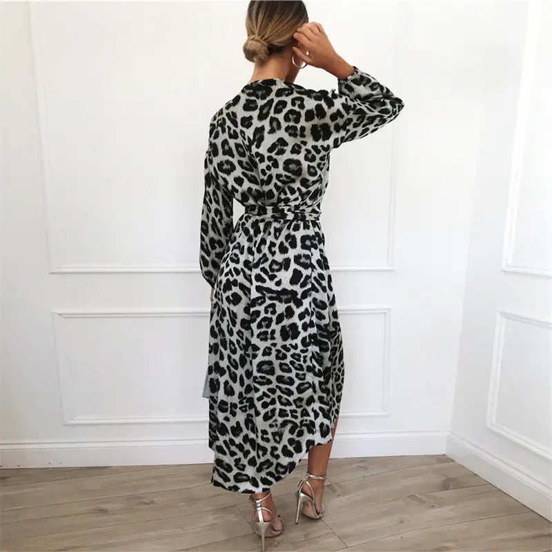 A woman wearing a long-sleeved belted leopard print chiffon wrap dress with a v neck and asymmetrical hemline.