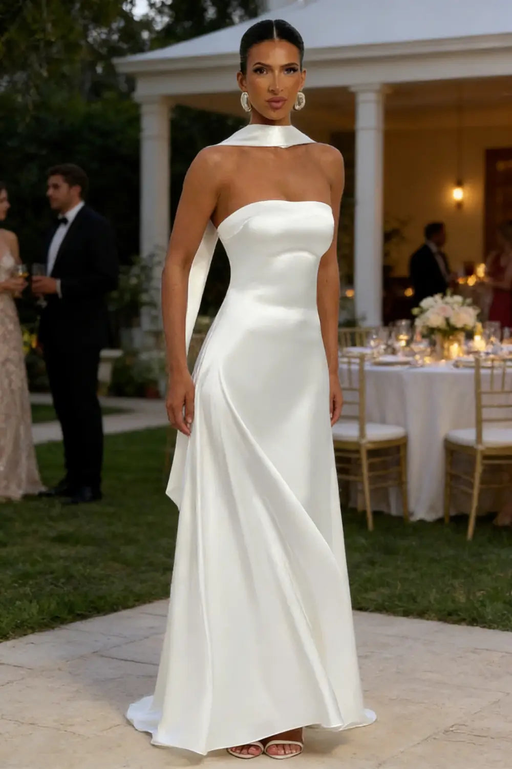 Un vestido de noche sin tirantes de satén blanco, de líneas elegantes, con detalle drapeado en el hombro y silueta fluida.