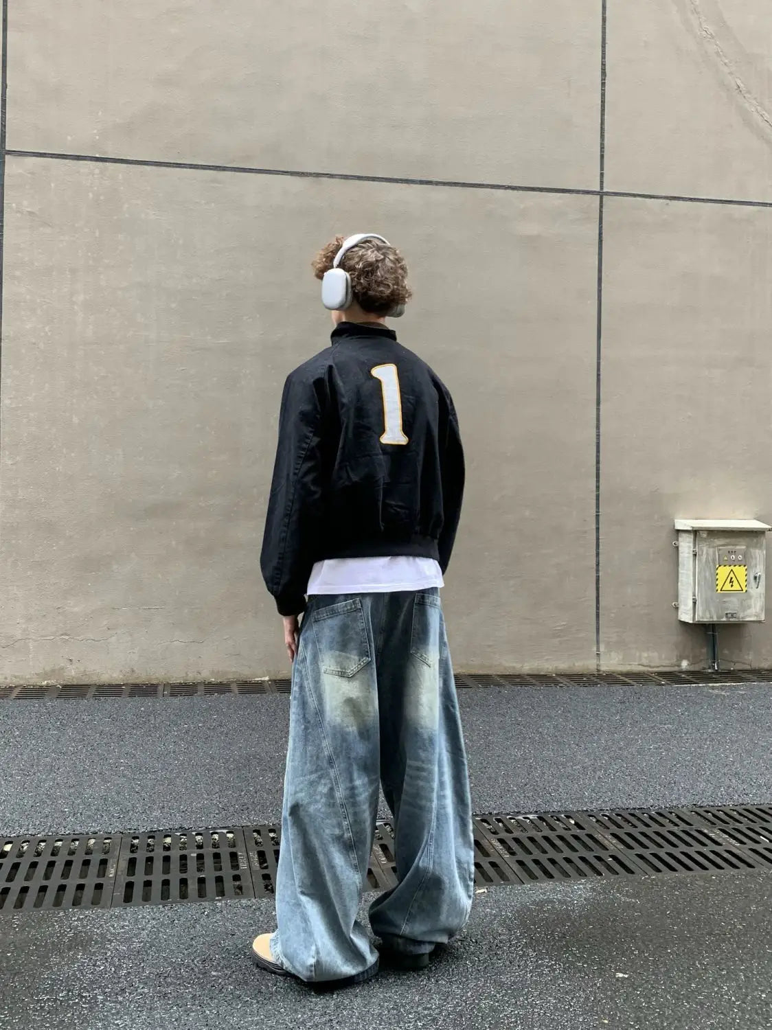Parte trasera de una chaqueta bomber negra con el número blanco 1, que presenta un estilo de chaqueta corta tipo béisbol azul marino con cuello de piel.