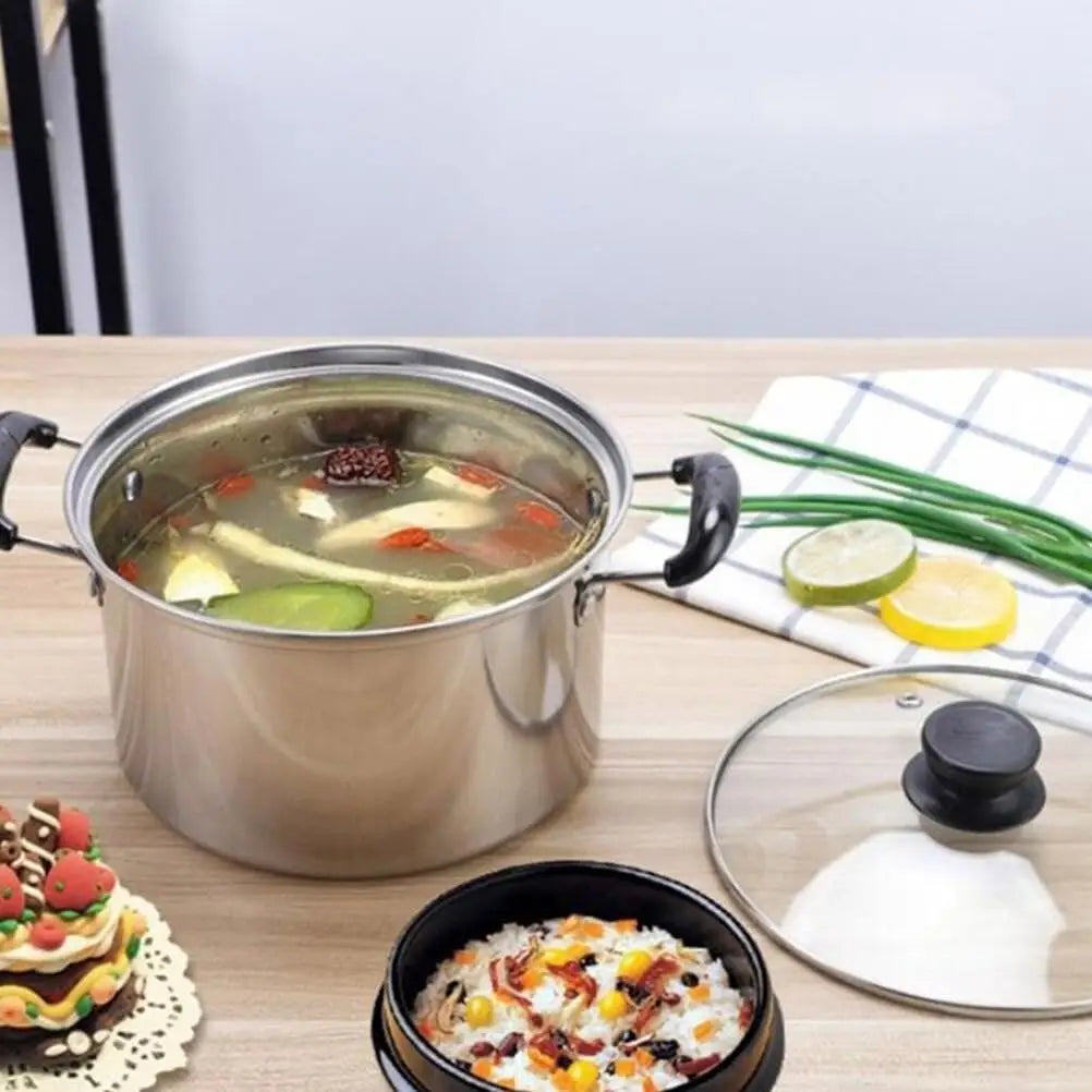 Stainless steel induction cookware set 5 pieces featuring a stainless steel pot with black handles and a glass lid filled with clear broth containing vegetables and herbs.