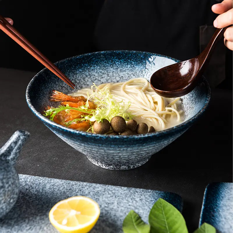 A deep blue speckled ceramic ramen bowl filled with noodles shrimp and mushrooms for kitchenware use.