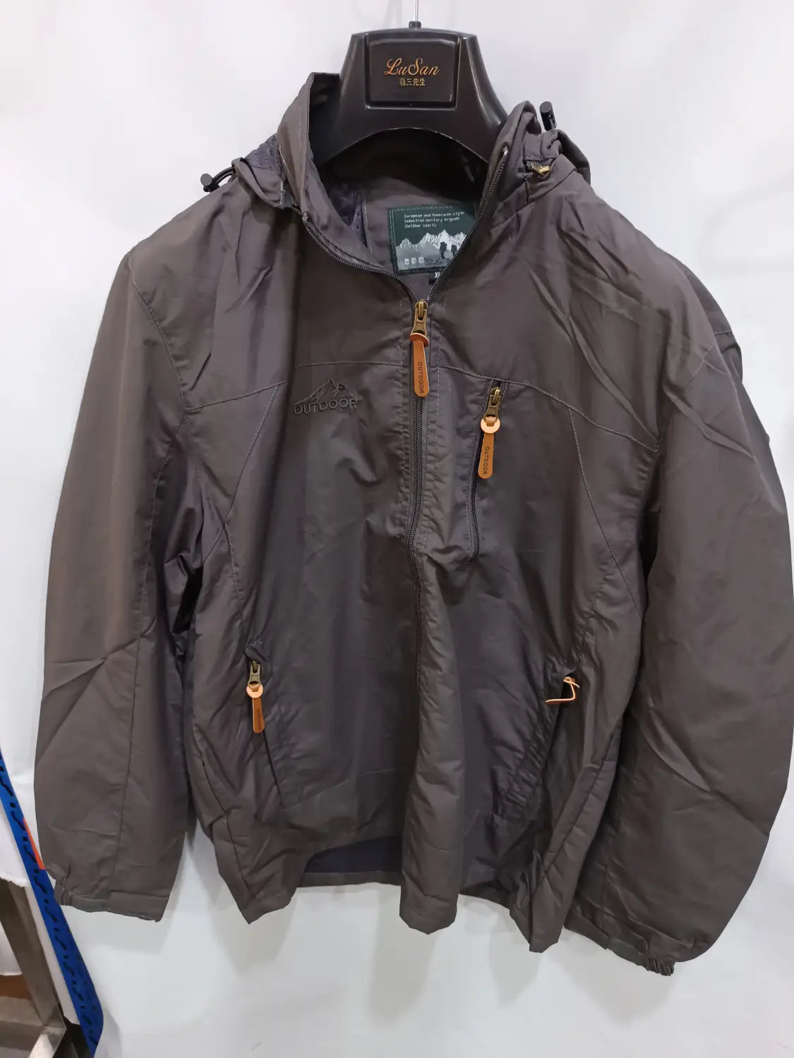 Chaqueta de senderismo con capucha impermeable color gris oscuro, con cierre frontal mediante cremallera y múltiples bolsillos con cremalleras, con tiradores de cuero color camel.