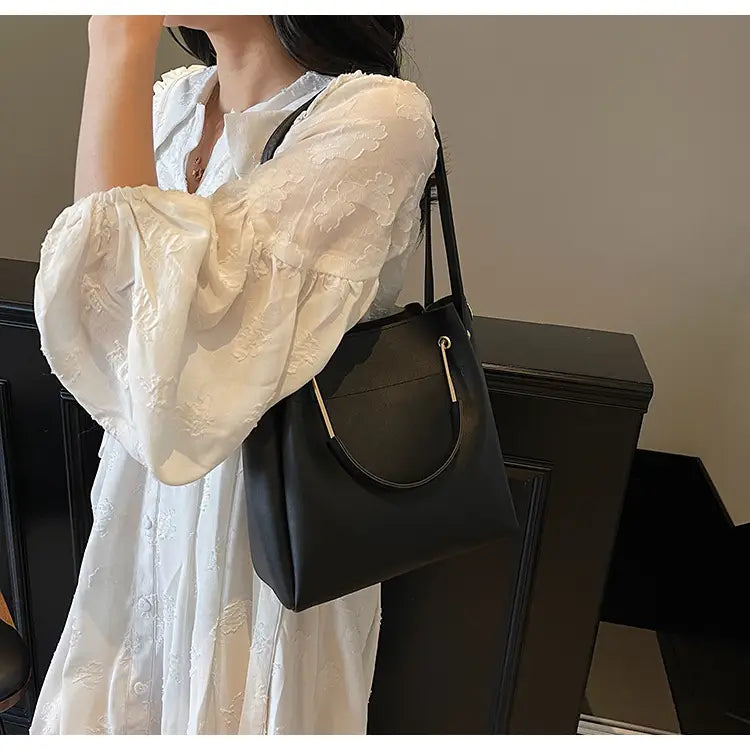 Black leather minimalist bucket bag with gold-tone hardware, top handle, and detachable strap.