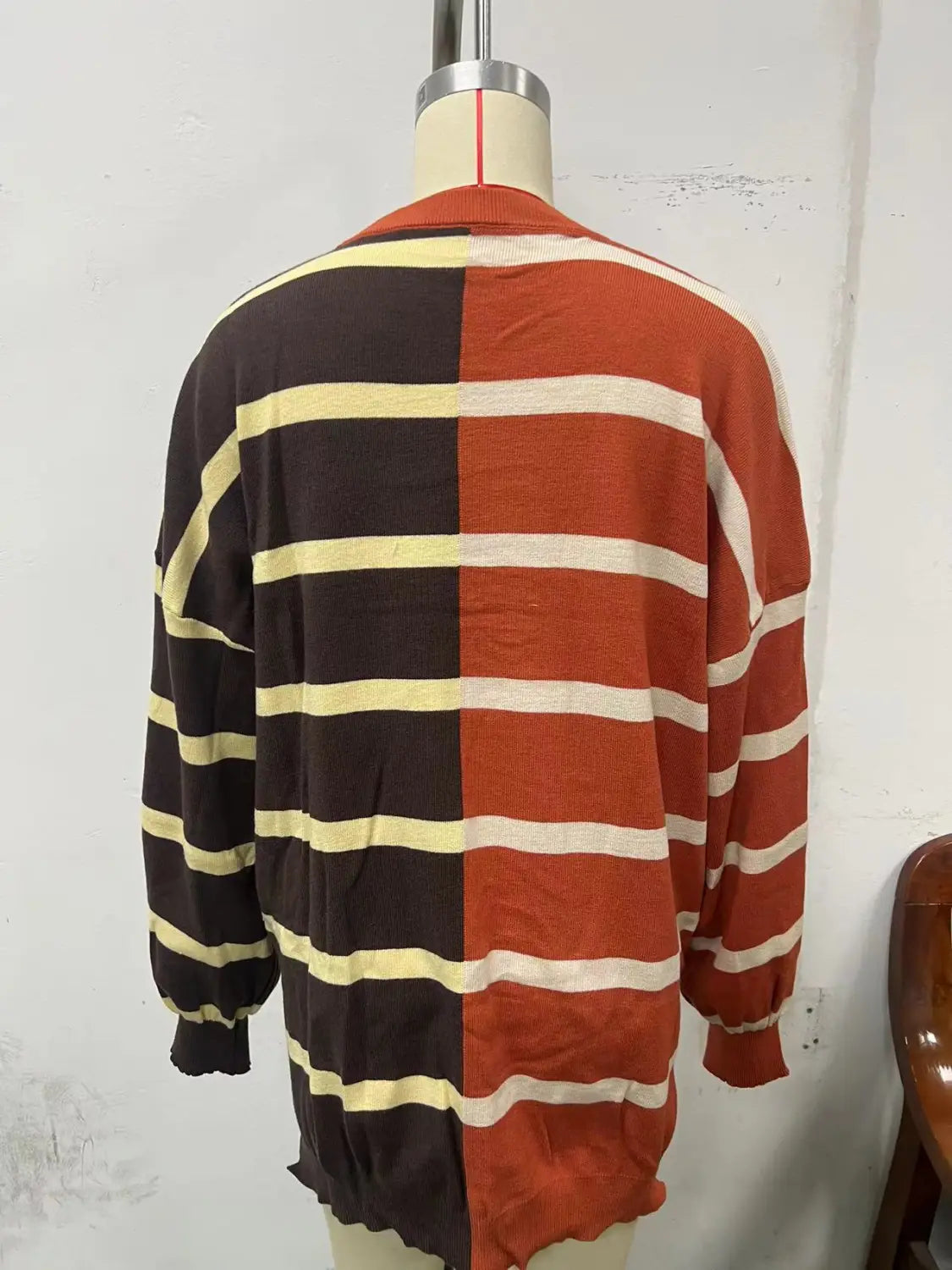 women’s oversized split color striped knit sweater featuring dark brown and cream stripes on one side and rust orange and off-white stripes on the other side.
