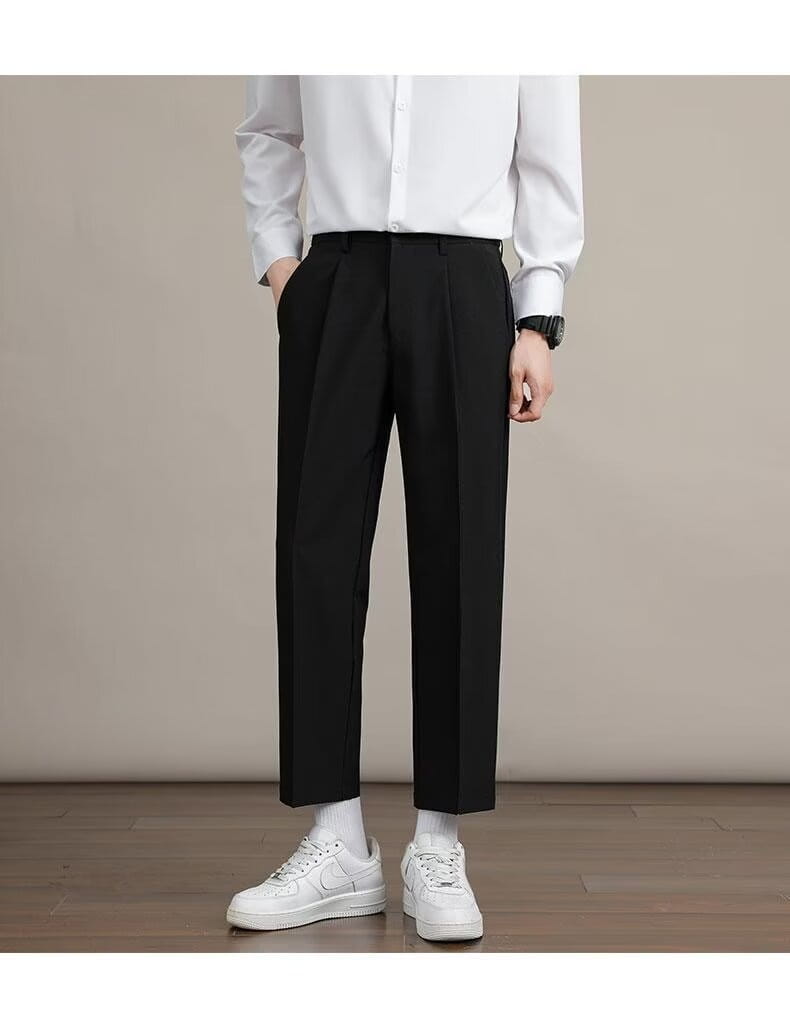黒のメンズ用ミニマリスト・ストレートカットのドレスパンツ。プリーツ仕様のストレートレッグのカットと、クロップド丈の裾を備えたフォーマルウェア向けです。