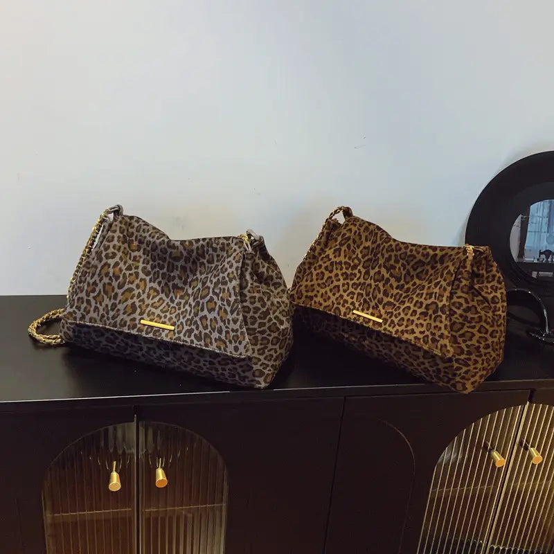 Two leopard print crossbody bags with gold chain straps in muted brownish gray and richer golden brown hues featuring gold tone hardware.