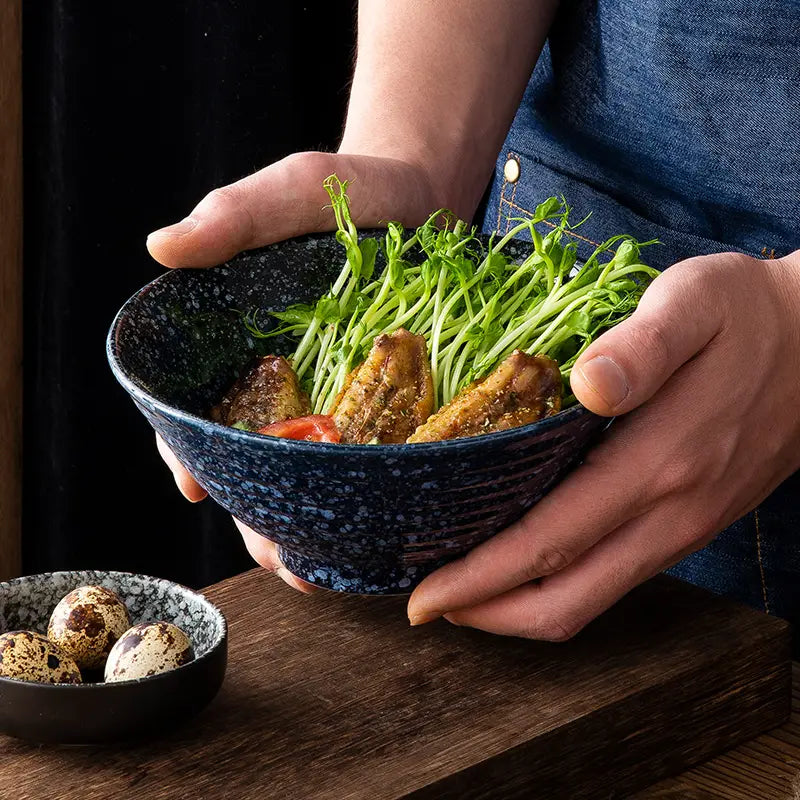 Eine tiefblaue, gesprenkelte Keramikschale aus einem Set „japanische Keramikschalen – rustikal gesprenkelt“ mit Tischgeschirr, gefüllt mit einem lebendigen Salat aus grünen Sprossen und gegrilltem Hähnchen.