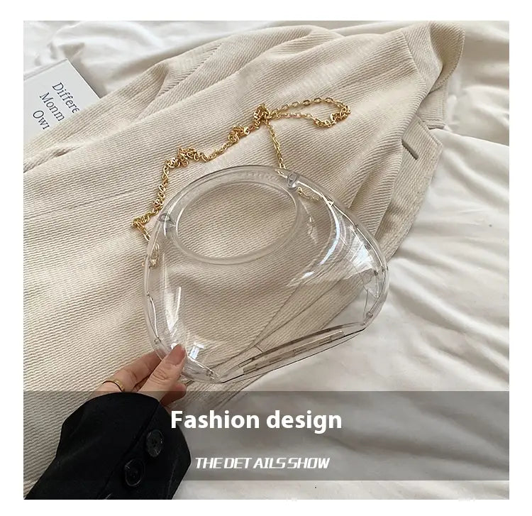 Clear acrylic handbag with a gold metallic chain strap designed as a geometric clutch bag.